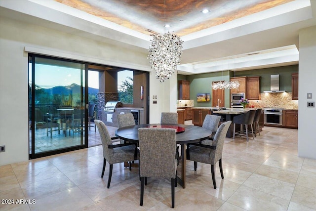 dining room with a tray ceiling, a mountain view, sink, and a chandelier