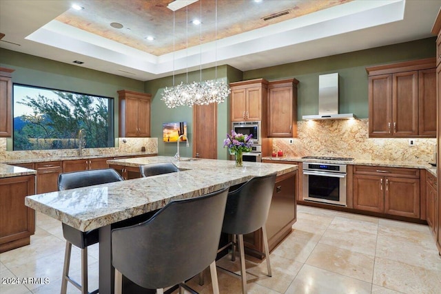 kitchen featuring sink, stainless steel appliances, wall chimney range hood, a raised ceiling, and a kitchen breakfast bar