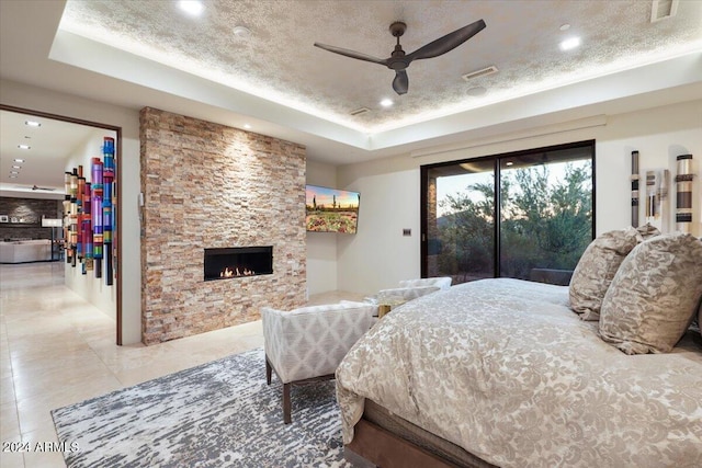 bedroom with access to outside, ceiling fan, a fireplace, and a tray ceiling