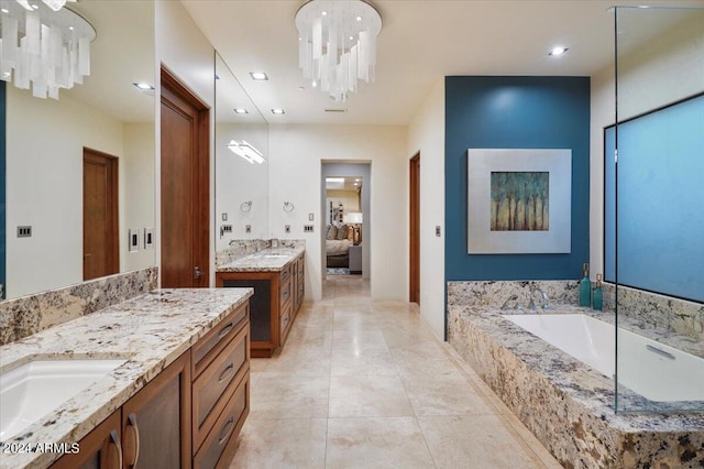 bathroom with a notable chandelier, vanity, and tiled bath