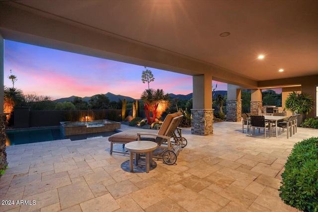 patio terrace at dusk with a mountain view and a swimming pool with hot tub