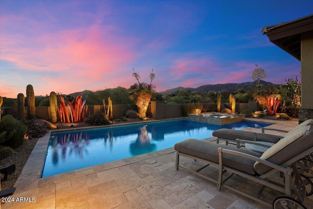 pool at dusk featuring an in ground hot tub, a mountain view, and a patio