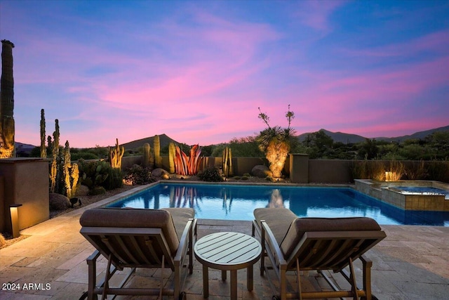 pool at dusk with an in ground hot tub and a patio