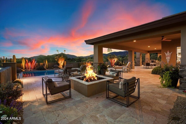 patio terrace at dusk featuring a fenced in pool, a mountain view, ceiling fan, and a fire pit