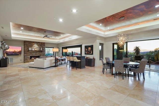 dining space featuring a fireplace, ceiling fan with notable chandelier, and a tray ceiling