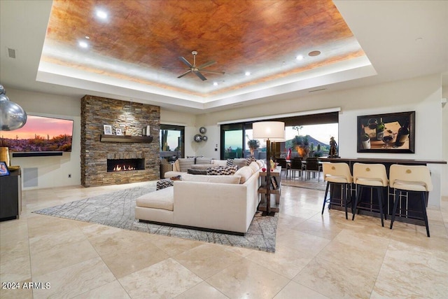 living room featuring a tray ceiling, ceiling fan, and a fireplace