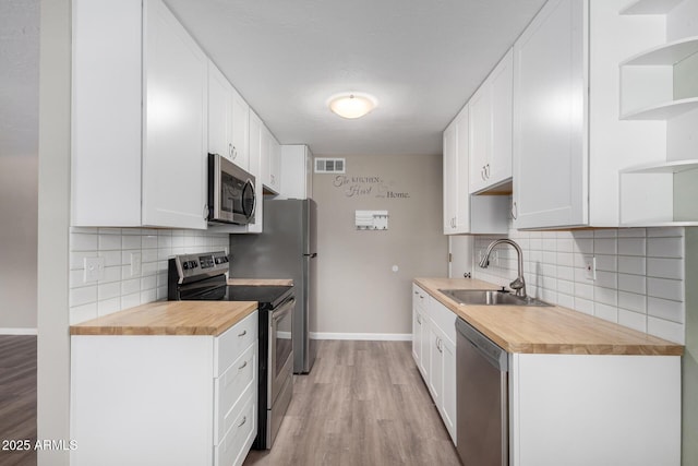 kitchen with white cabinetry, butcher block counters, appliances with stainless steel finishes, light wood-type flooring, and sink