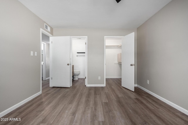 unfurnished bedroom with ensuite bathroom, a closet, a spacious closet, and dark wood-type flooring