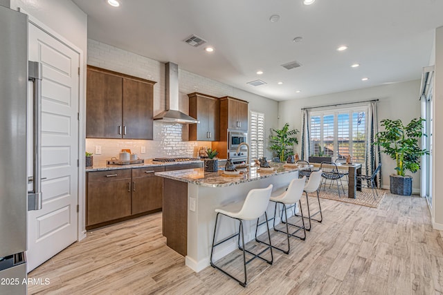 17831 W Mission Ln, Waddell, AZ 85355 - kitchen featuring visible vents, light stone countertops, a breakfast bar area, wall chimney range hood, and light wood finished floors