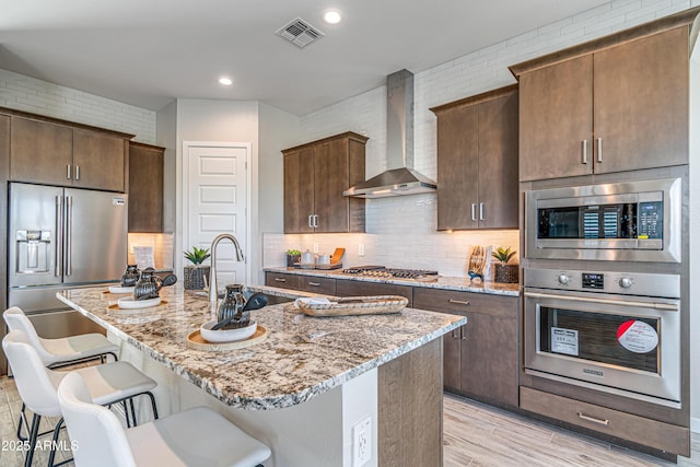 17831 W Mission Ln, Waddell, AZ 85355 - kitchen with visible vents, a breakfast bar, wall chimney range hood, light stone counters, and appliances with stainless steel finishes