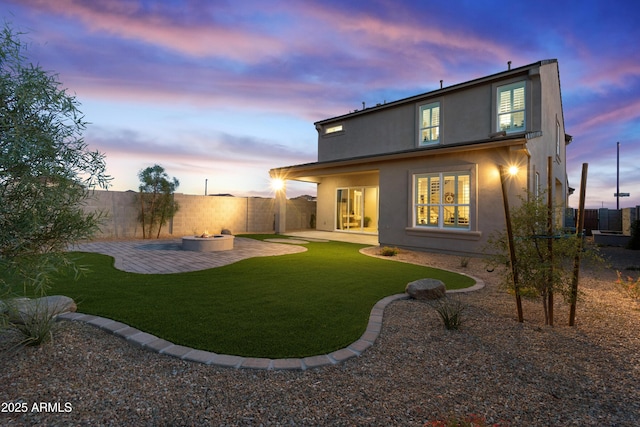 17831 W Mission Ln, Waddell, AZ 85355 - back of house at dusk featuring stucco siding, a fenced backyard, a patio area, a lawn, and a fire pit