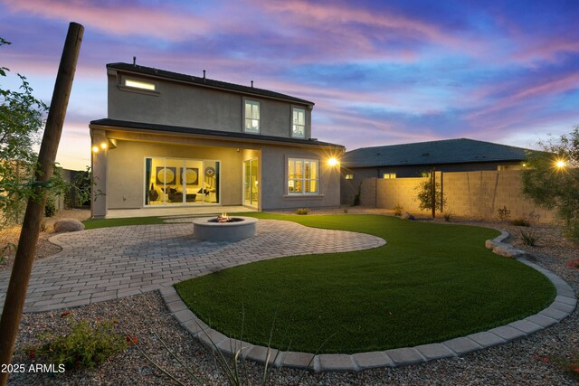 17831 W Mission Ln, Waddell, AZ 85355 - back of house at dusk with an outdoor fire pit, stucco siding, a fenced backyard, a lawn, and a patio