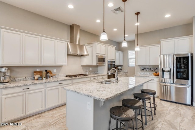 kitchen featuring wall chimney range hood, hanging light fixtures, an island with sink, sink, and stainless steel appliances