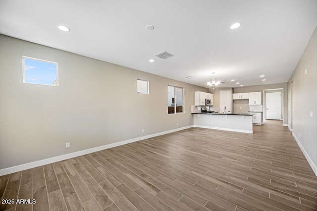 unfurnished living room with a chandelier, visible vents, baseboards, and wood finished floors