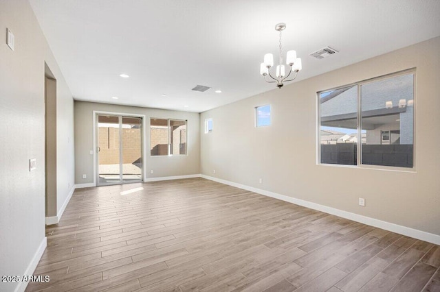 spare room featuring a notable chandelier, visible vents, baseboards, and wood finished floors