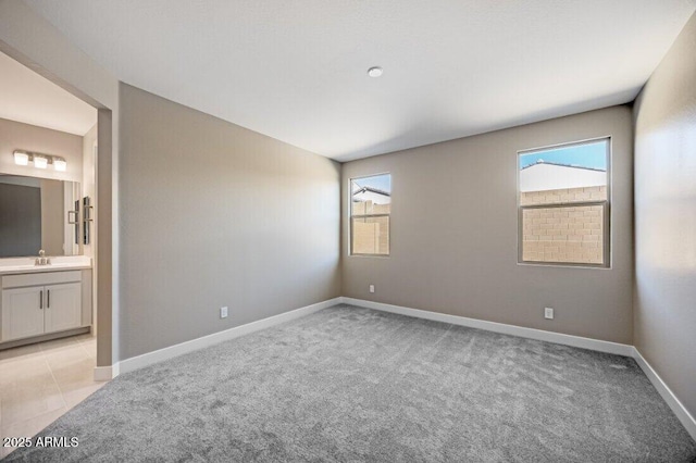 unfurnished bedroom with light carpet, baseboards, and a sink