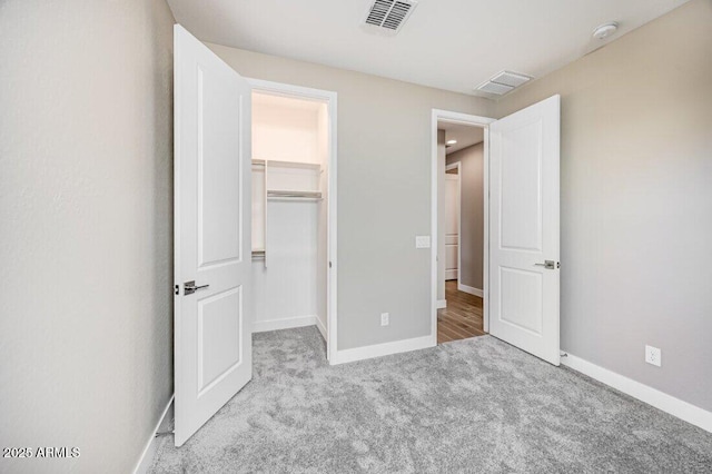 unfurnished bedroom with carpet floors, a spacious closet, visible vents, and baseboards