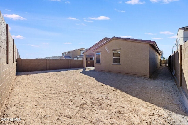 rear view of house with a tiled roof, a fenced backyard, and stucco siding