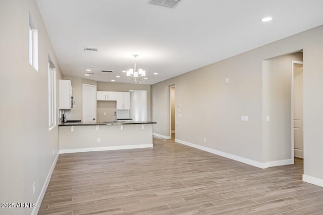 kitchen featuring a peninsula, a sink, white cabinetry, light wood-type flooring, and dark countertops