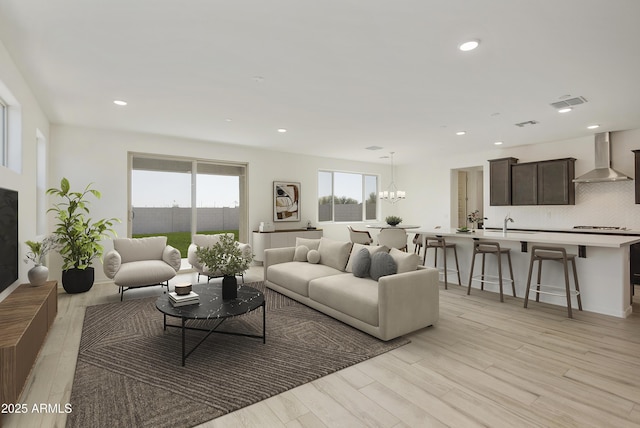living area with a fireplace, recessed lighting, visible vents, light wood-style floors, and a chandelier