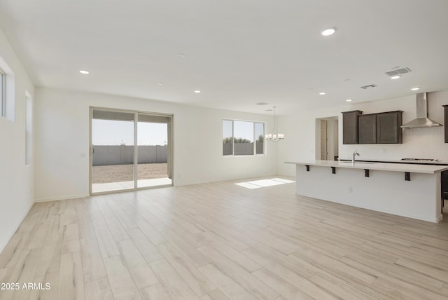 unfurnished living room featuring recessed lighting, visible vents, baseboards, light wood finished floors, and an inviting chandelier