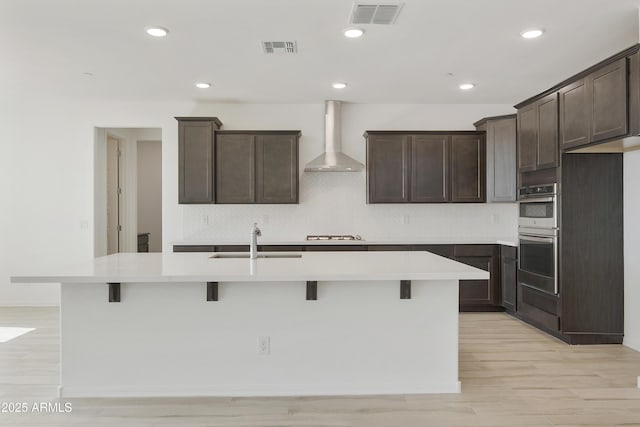 kitchen with visible vents, a sink, wall chimney exhaust hood, and dark brown cabinets