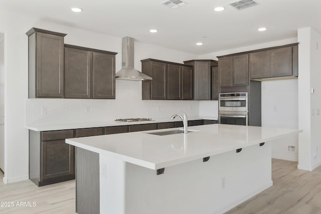 kitchen with stainless steel appliances, wall chimney range hood, a sink, and visible vents