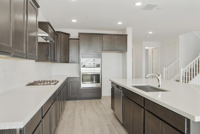 kitchen featuring stainless steel appliances, a sink, dark brown cabinets, light countertops, and backsplash