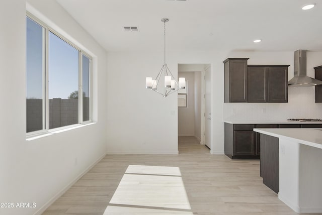 kitchen with light wood finished floors, wall chimney exhaust hood, visible vents, and dark brown cabinets