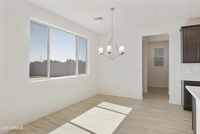 unfurnished dining area featuring a chandelier, light wood finished floors, visible vents, and baseboards