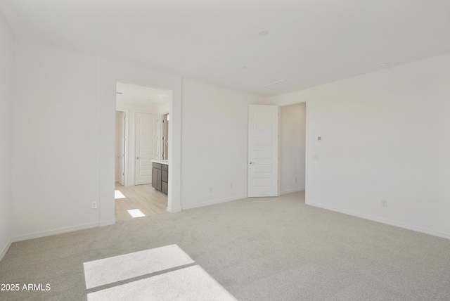 unfurnished bedroom featuring light colored carpet, ensuite bath, and baseboards