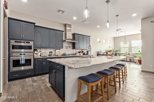 kitchen featuring a spacious island, pendant lighting, appliances with stainless steel finishes, and wall chimney exhaust hood