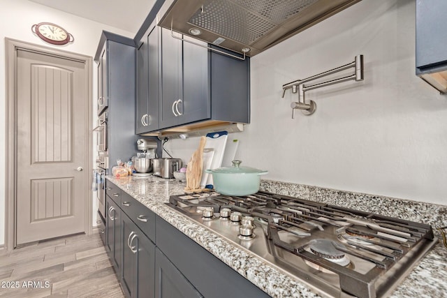 kitchen with light stone countertops, stainless steel gas stovetop, and light wood-type flooring