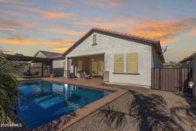 back house at dusk with a fenced in pool and a patio area