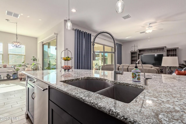 kitchen featuring dishwasher, hanging light fixtures, light stone countertops, ceiling fan with notable chandelier, and sink