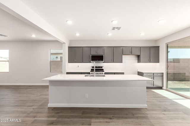 kitchen featuring a center island with sink, appliances with stainless steel finishes, light wood-type flooring, and gray cabinets