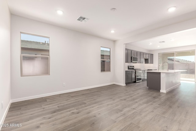 kitchen featuring stainless steel appliances, wood-type flooring, a healthy amount of sunlight, and a kitchen island with sink