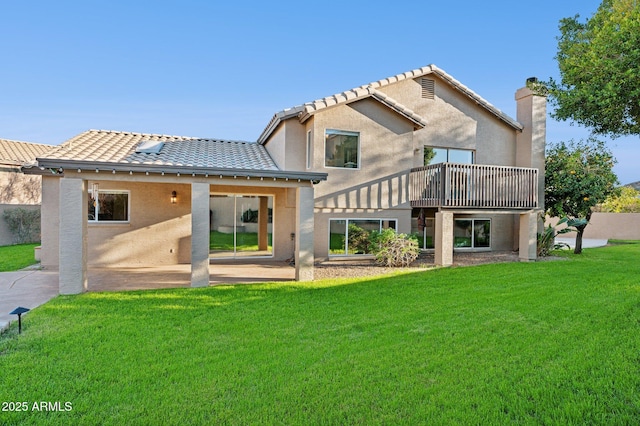 rear view of house featuring a tiled roof, a chimney, a lawn, and stucco siding