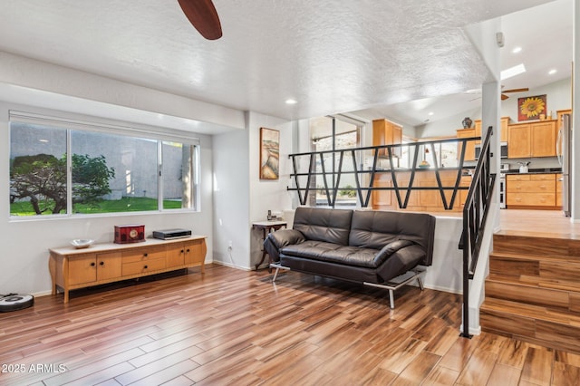 living area with lofted ceiling, ceiling fan, a textured ceiling, light wood-style flooring, and stairway