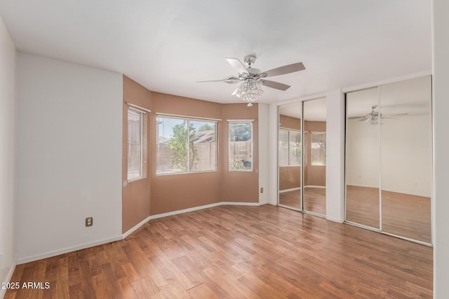 12425 W Willow Ave, El Mirage, AZ 85335 - unfurnished bedroom with two closets, wood finished floors, baseboards, and a ceiling fan