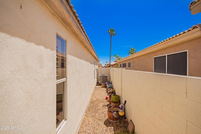 view of side of home featuring stucco siding, central air condition unit, and fence