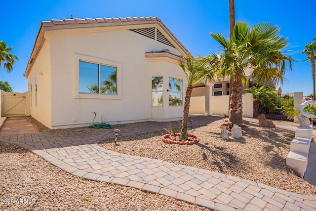 view of front of property with fence, a tile roof, stucco siding, a gate, and a patio