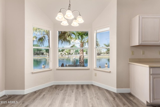 unfurnished dining area featuring light wood-style floors, a water view, lofted ceiling, and a notable chandelier