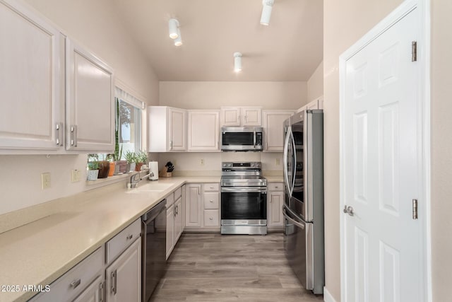 kitchen with light countertops, white cabinets, a sink, light wood-style flooring, and stainless steel appliances