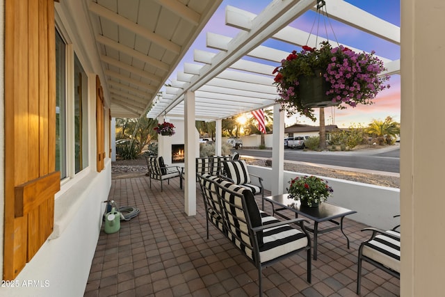 patio terrace at dusk featuring an outdoor fireplace and a pergola