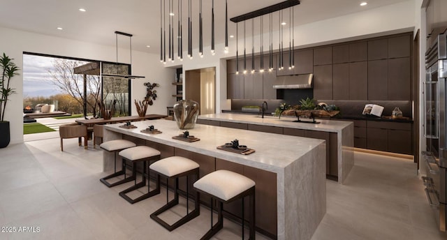 kitchen with modern cabinets, a center island with sink, under cabinet range hood, a sink, and decorative light fixtures