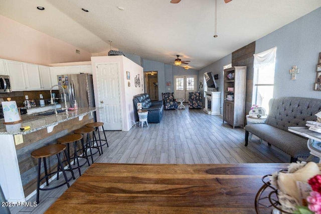 living area featuring ceiling fan, vaulted ceiling, and light wood finished floors