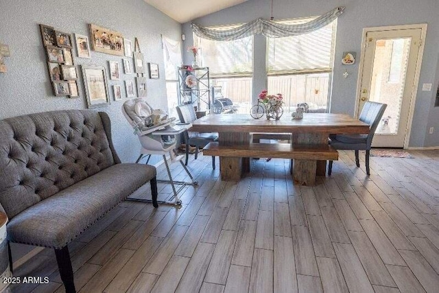 dining space with wood finished floors, vaulted ceiling, and a textured wall