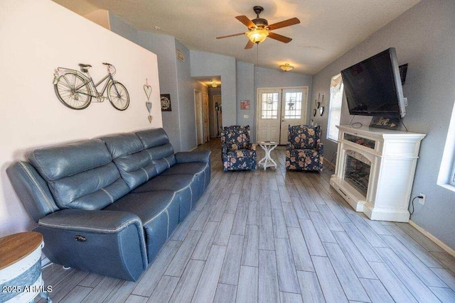 living room with wood finished floors, a ceiling fan, lofted ceiling, a fireplace with raised hearth, and baseboards