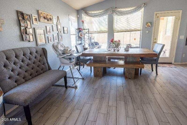dining room featuring wood finished floors, lofted ceiling, and a textured wall